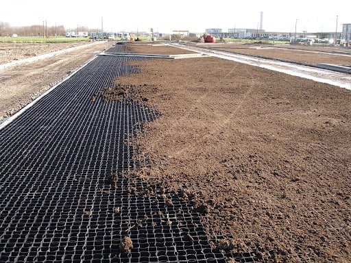 A long strip of black Ecoraster permeable paving partially covered with brown growing medium.