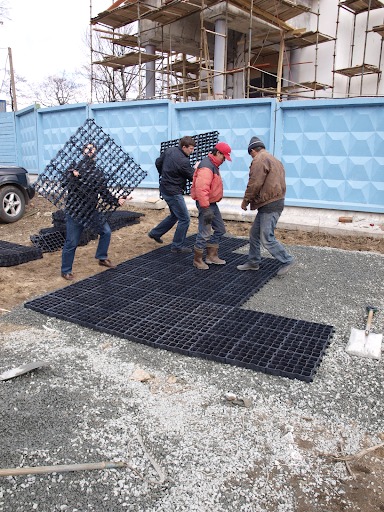 Several men installing Ecoraster grid tiles over grey gravel.