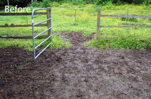 A horse paddock in a grassy area with an open metal gate. The horse paddock is filled with lumpy, uneven mud prior to the installation of permeable paving.